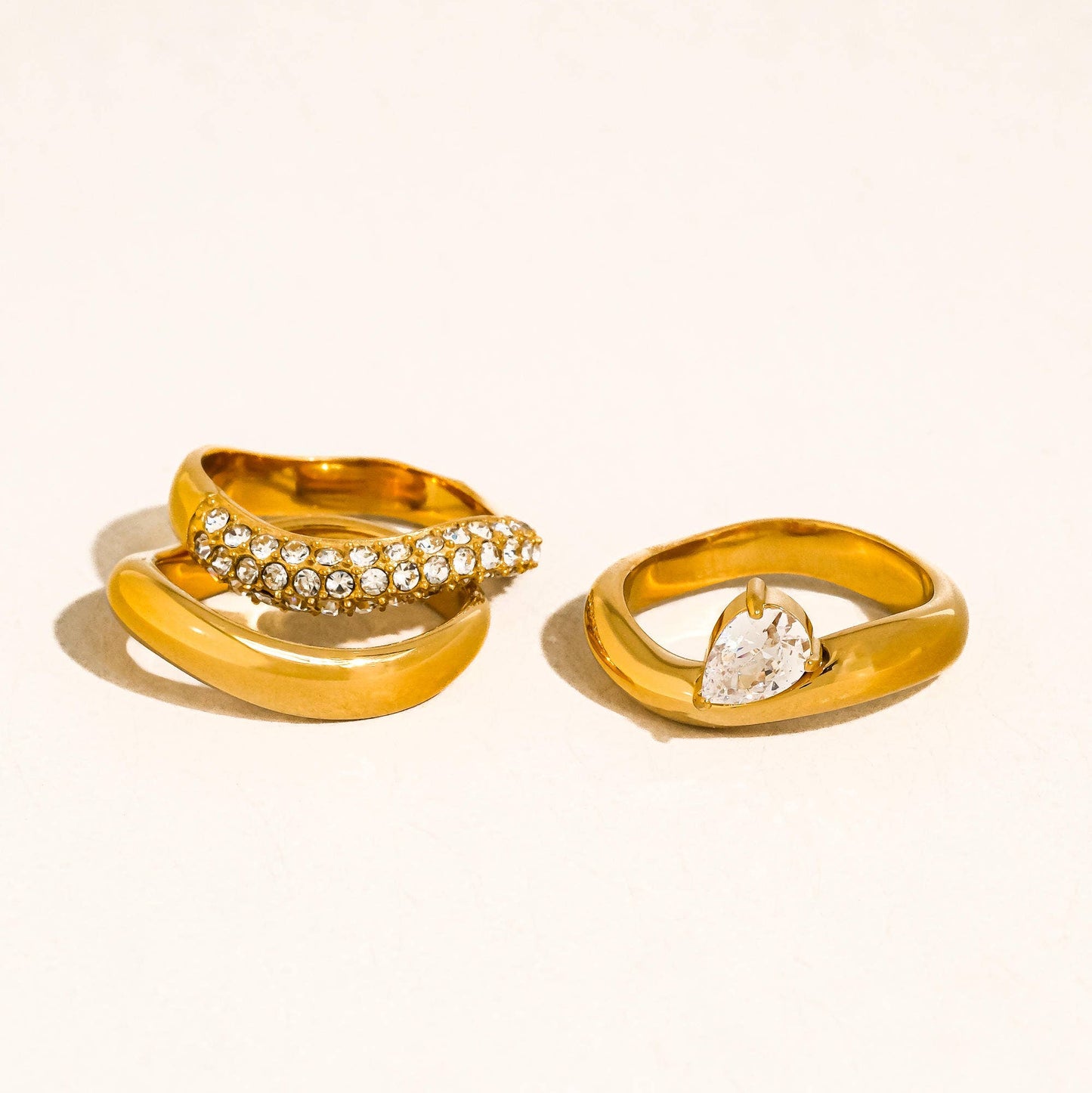 three gold rings with gemstones on a light beige background