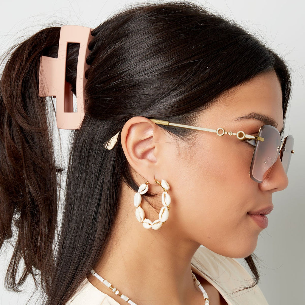 Woman wearing sunglasses, hoop earrings, and a necklace with a neutral background