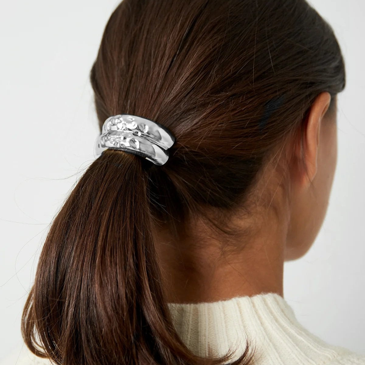 Person with a ponytail wearing a decorative hair tie against a plain background