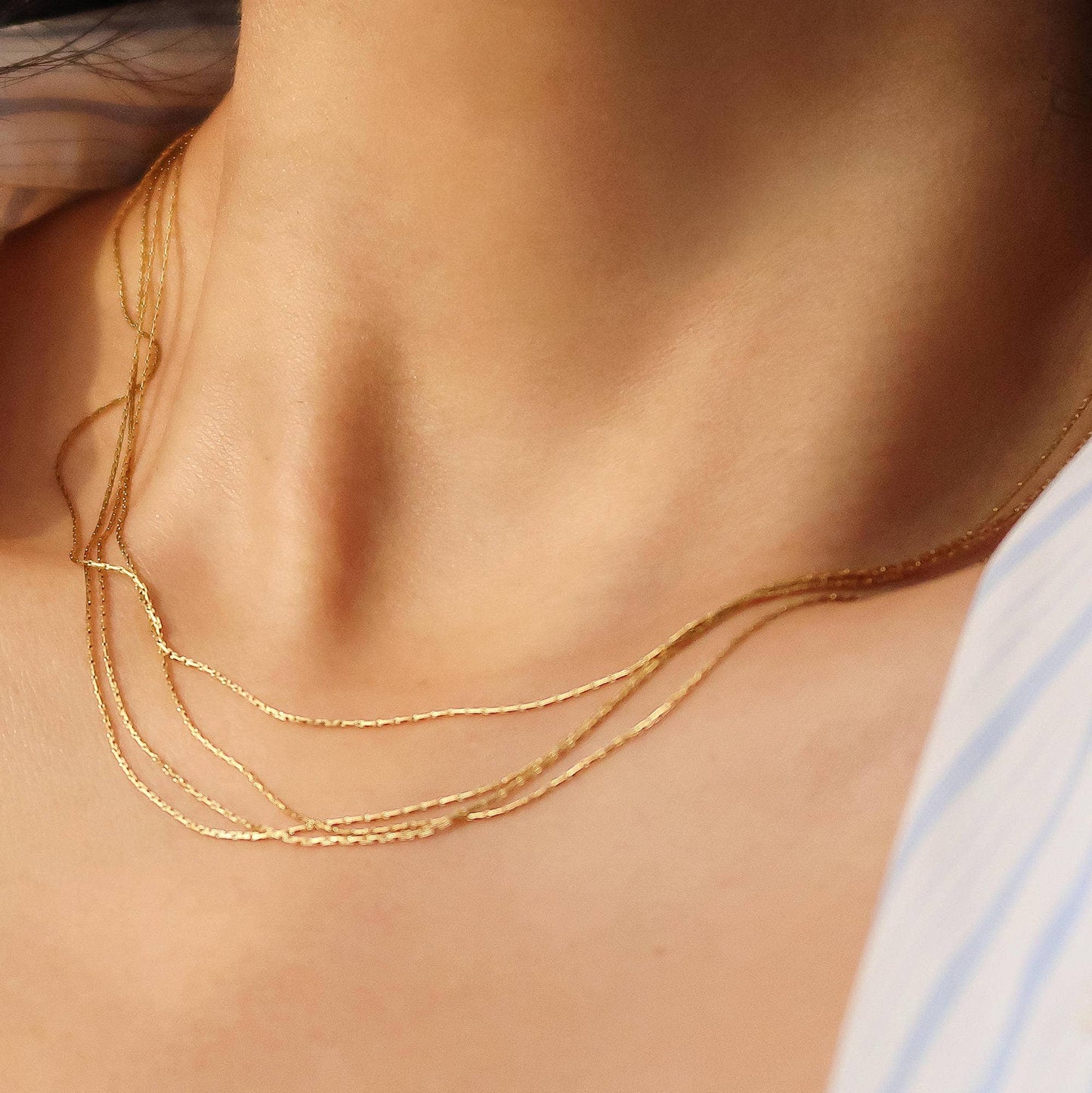 Close-up of a person wearing a gold necklace with a soft focus on the background