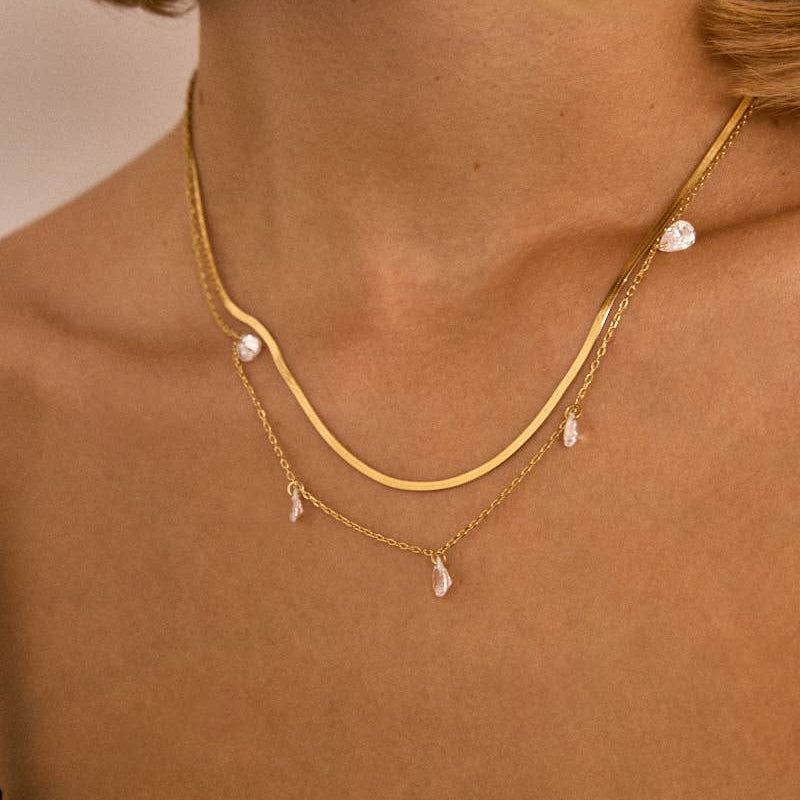 Gold necklace with pearl drops worn by a person against a neutral background