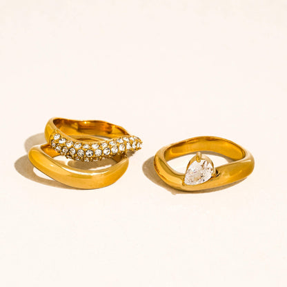 three gold rings with gemstones on a light beige background